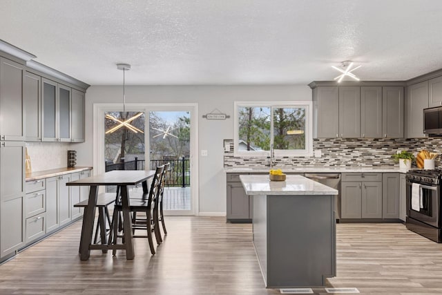 kitchen with gray cabinetry, decorative backsplash, stainless steel appliances, and light wood-style flooring