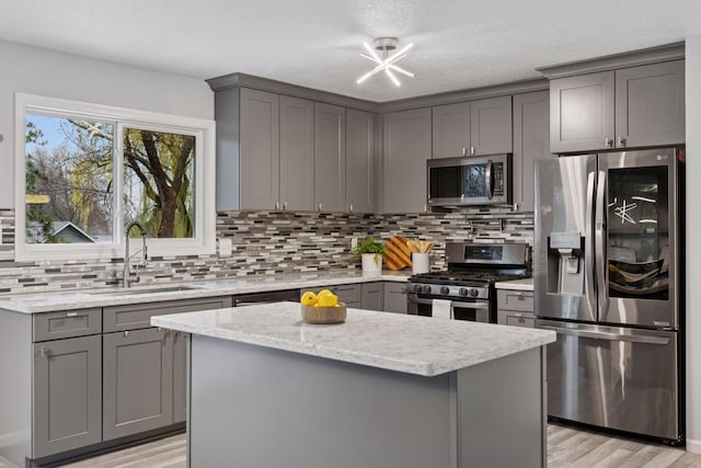 kitchen featuring decorative backsplash, light stone countertops, gray cabinetry, a sink, and stainless steel appliances