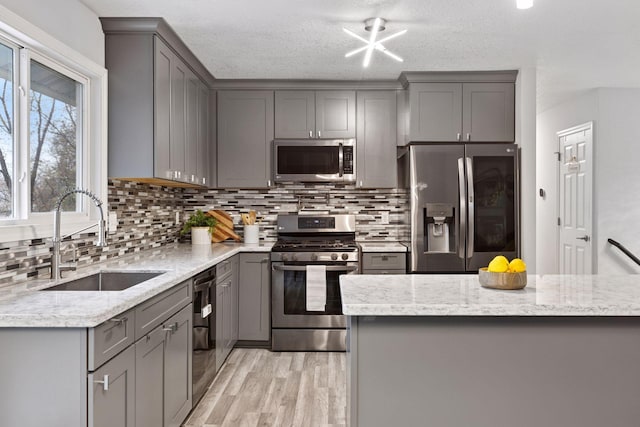 kitchen with gray cabinets, a sink, light stone counters, light wood finished floors, and stainless steel appliances