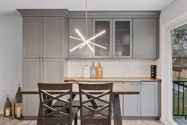 bar with a bar, backsplash, a wealth of natural light, and light wood-style flooring