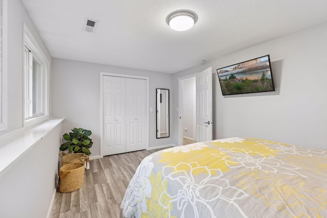 bedroom with visible vents, baseboards, wood finished floors, and a closet