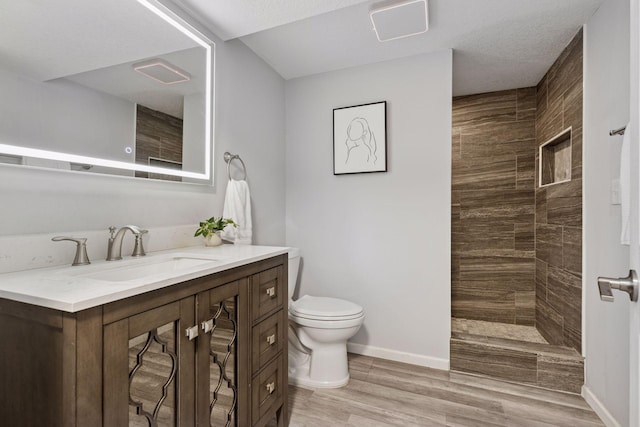 bathroom with vanity, baseboards, a tile shower, and toilet