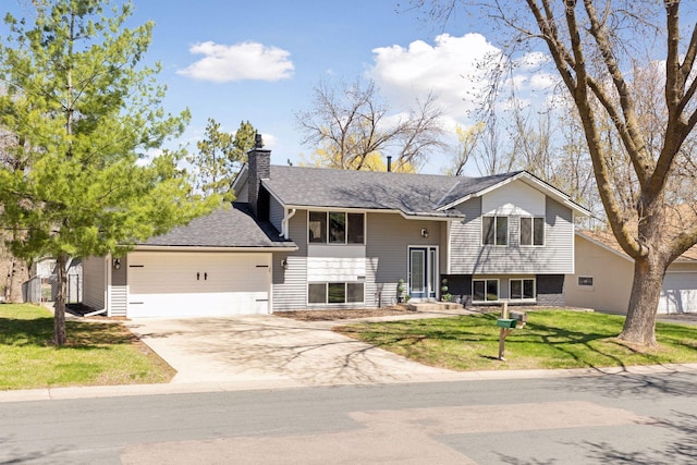 bi-level home with concrete driveway, a chimney, a front yard, and a garage