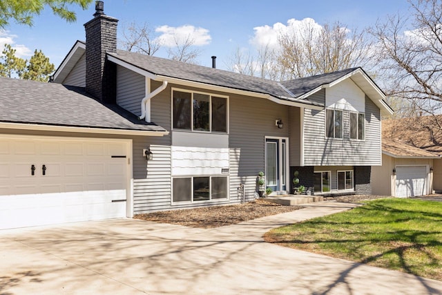 bi-level home with concrete driveway, an attached garage, a chimney, and a shingled roof