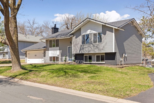 split foyer home with a chimney, a shingled roof, a front yard, and a garage