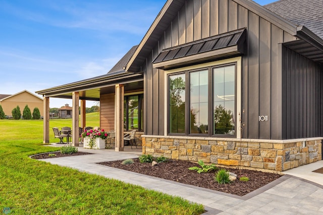 property entrance featuring a standing seam roof, stone siding, board and batten siding, and a lawn