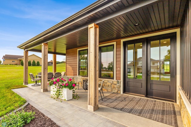 doorway to property with covered porch, stone siding, and a lawn