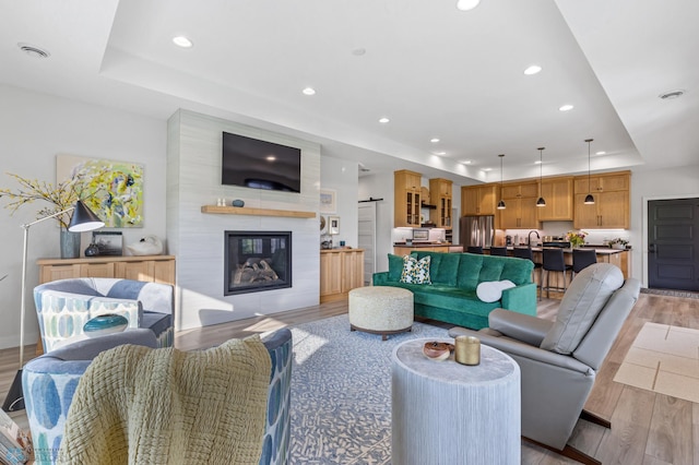 living room featuring recessed lighting, a fireplace, visible vents, a tray ceiling, and light wood finished floors