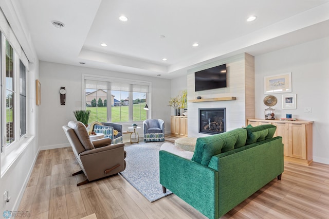 living room featuring light wood-style flooring, a fireplace, visible vents, baseboards, and a tray ceiling