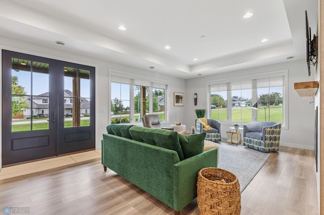 living area with light wood-type flooring, plenty of natural light, a tray ceiling, and french doors