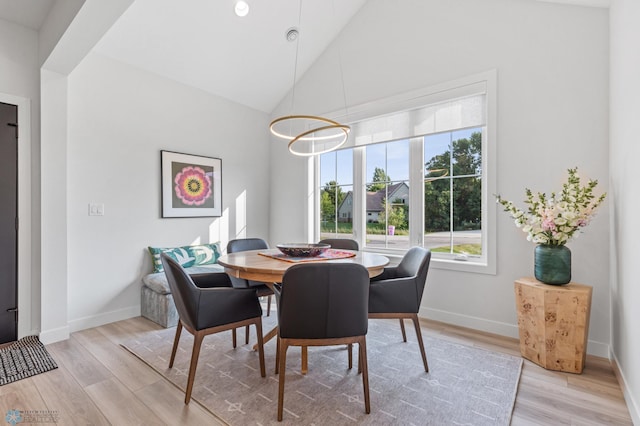 dining room with light wood finished floors, baseboards, and high vaulted ceiling