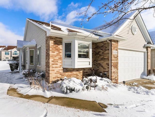 view of snowy exterior with an attached garage and brick siding