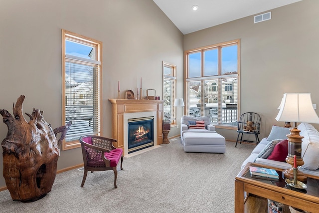 living room with visible vents, baseboards, a fireplace with flush hearth, carpet, and high vaulted ceiling