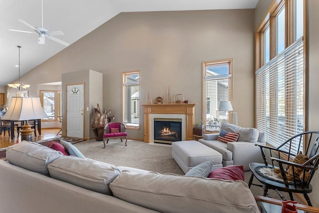 living area with high vaulted ceiling, a healthy amount of sunlight, a fireplace, and ceiling fan with notable chandelier