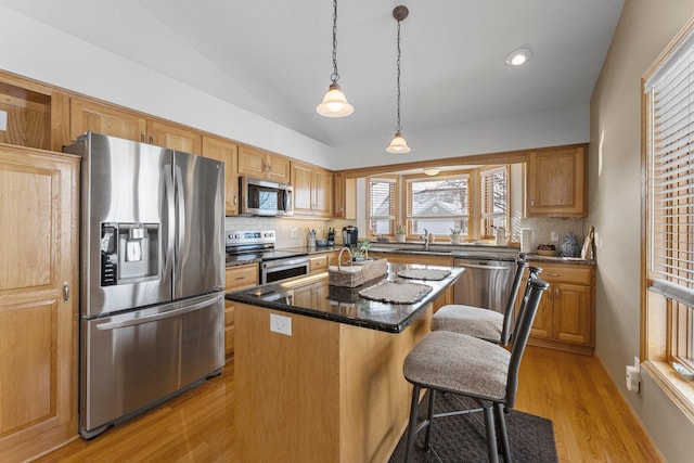 kitchen featuring light wood finished floors, appliances with stainless steel finishes, a sink, vaulted ceiling, and a kitchen island