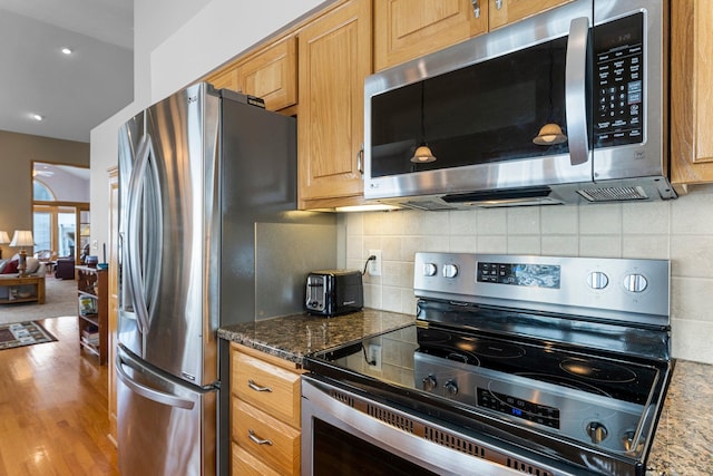 kitchen featuring dark stone countertops, appliances with stainless steel finishes, backsplash, and wood finished floors