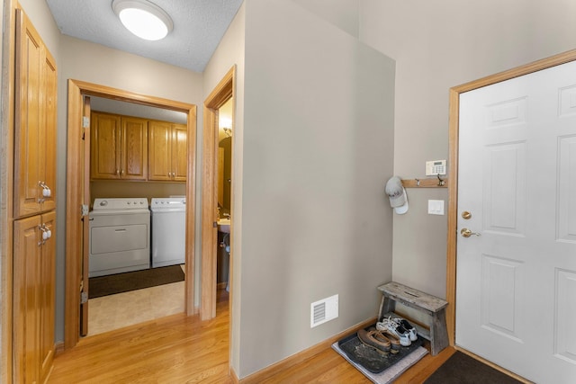 foyer entrance featuring visible vents, light wood-style flooring, washing machine and dryer, a textured ceiling, and baseboards