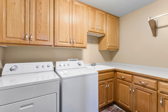 laundry area with a textured ceiling, washing machine and dryer, a sink, and cabinet space