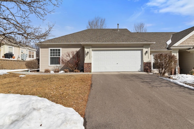 ranch-style home with a garage, brick siding, roof with shingles, and driveway