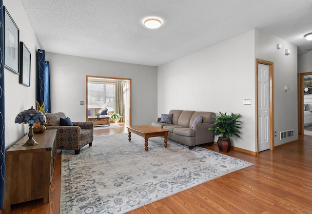 living room featuring visible vents, a textured ceiling, baseboards, and wood finished floors