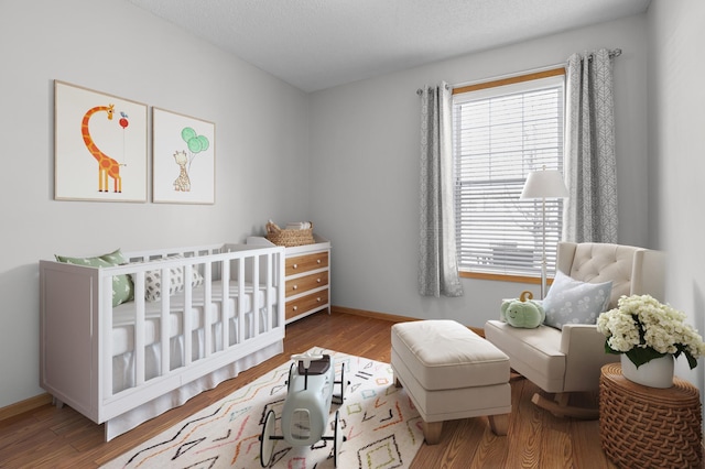 bedroom featuring baseboards, a nursery area, and wood finished floors