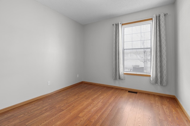 unfurnished room with a textured ceiling, baseboards, visible vents, and light wood-type flooring