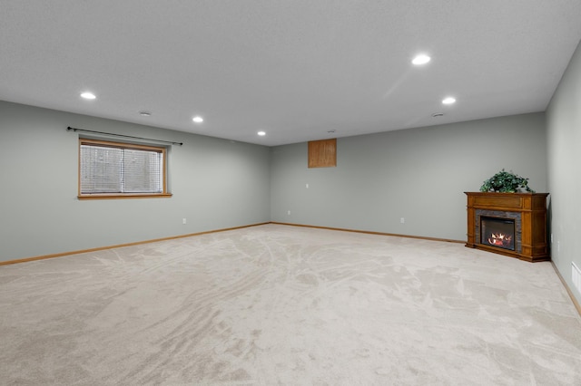 basement featuring recessed lighting, baseboards, light carpet, and a glass covered fireplace