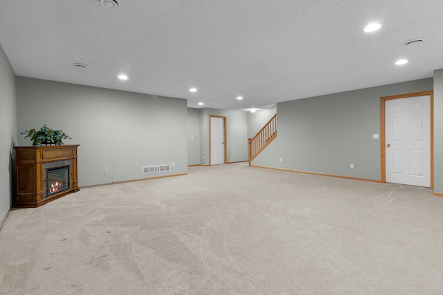 finished basement with visible vents, a glass covered fireplace, recessed lighting, stairway, and baseboards