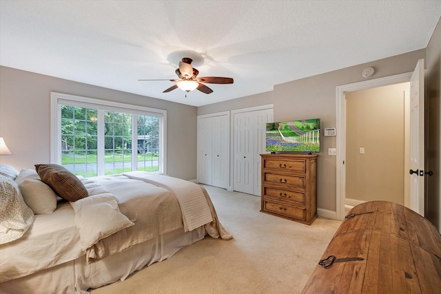 bedroom featuring multiple closets, light carpet, and a ceiling fan
