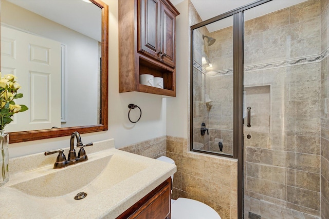 bathroom featuring a stall shower, tile walls, toilet, vanity, and wainscoting