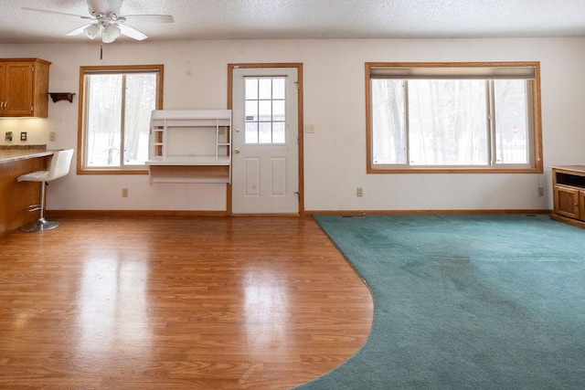 unfurnished living room with a ceiling fan, a textured ceiling, baseboards, and wood finished floors