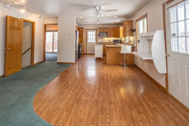 kitchen featuring appliances with stainless steel finishes, brown cabinets, wood finished floors, a peninsula, and light countertops