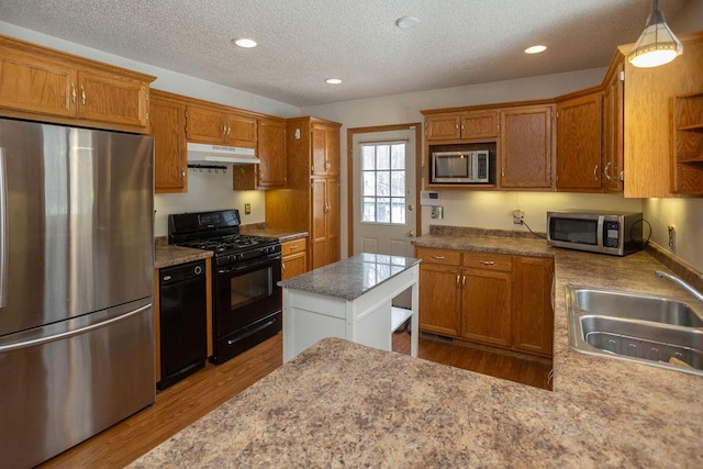 kitchen with wood finished floors, appliances with stainless steel finishes, a sink, and under cabinet range hood