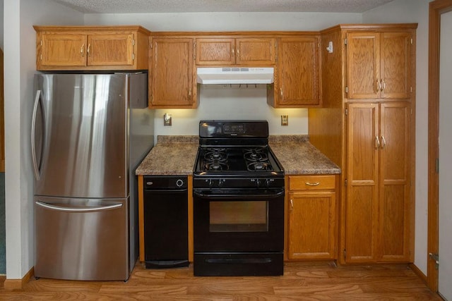 kitchen featuring under cabinet range hood, black gas stove, freestanding refrigerator, light wood finished floors, and brown cabinetry