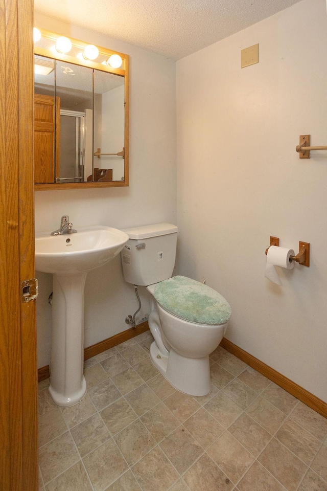 bathroom featuring a textured ceiling, toilet, a sink, baseboards, and an enclosed shower