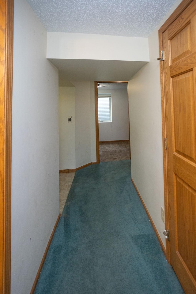 corridor featuring a textured ceiling, carpet flooring, and baseboards