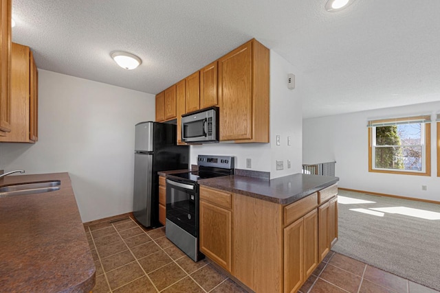 kitchen with dark countertops, open floor plan, stainless steel appliances, dark carpet, and a sink