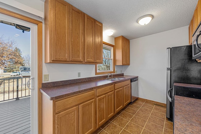 kitchen with dark countertops, a sink, a textured ceiling, dark tile patterned floors, and stainless steel dishwasher