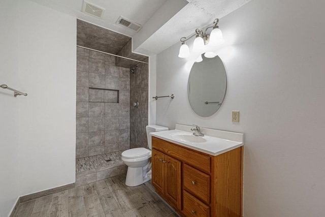 full bath featuring visible vents, toilet, wood finished floors, a tile shower, and vanity