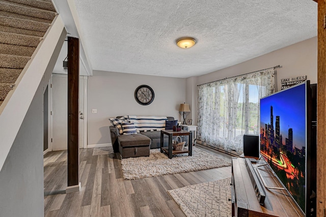 living room featuring baseboards, a textured ceiling, wood finished floors, and stairs