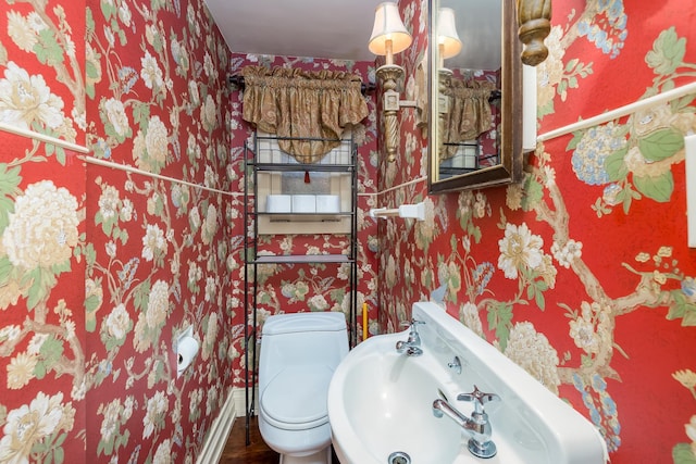 bathroom featuring toilet, wallpapered walls, and a sink