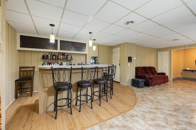 bar with decorative light fixtures, light wood finished floors, visible vents, a bar, and a drop ceiling