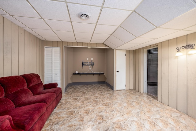 living area featuring a drop ceiling, visible vents, and wooden walls