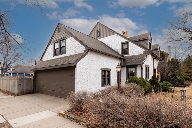 view of side of property featuring a garage, a shingled roof, concrete driveway, a chimney, and fence