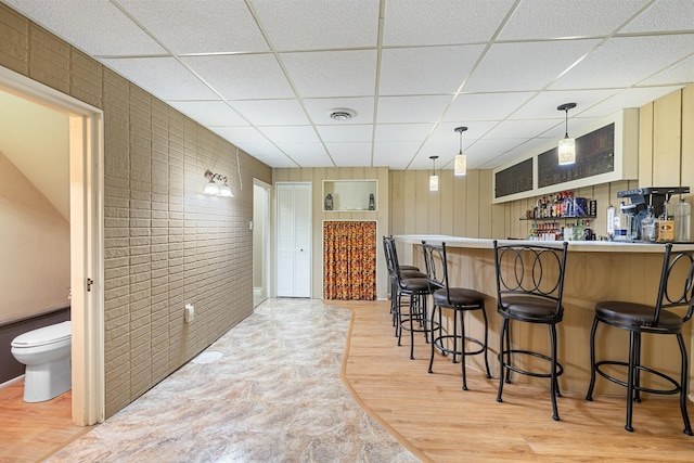 kitchen with a paneled ceiling, a breakfast bar, visible vents, and light wood-style floors