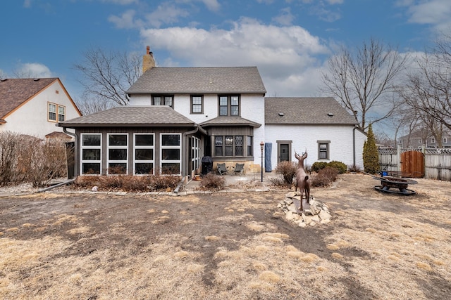 rear view of house with roof with shingles, brick siding, a chimney, a sunroom, and fence