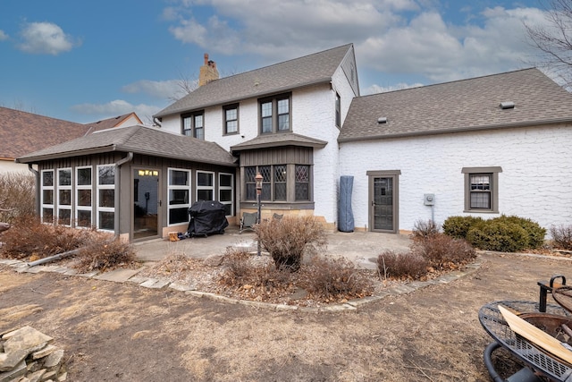 back of house featuring roof with shingles, a chimney, a patio area, and a sunroom