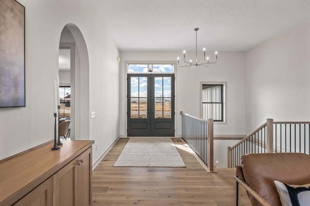 foyer with arched walkways, french doors, an inviting chandelier, light wood-style floors, and baseboards