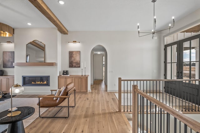 interior space featuring arched walkways, light wood finished floors, a glass covered fireplace, and beam ceiling