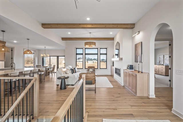 interior space with a chandelier, light wood-style flooring, recessed lighting, beamed ceiling, and a glass covered fireplace